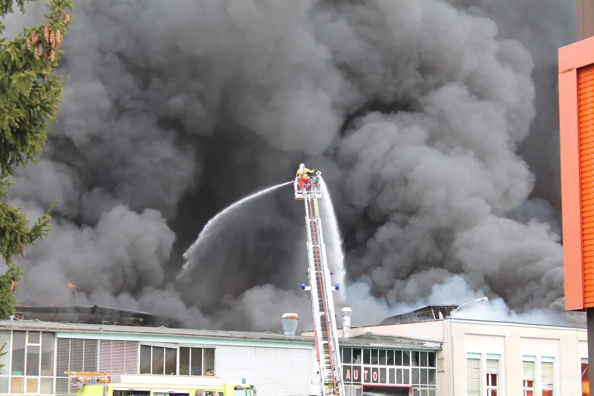 Löschender Feuerwehrmann vor riesiger Rauchwolke.